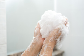 Hands woman millennial squeeze use foam taking shower. Female wash body with foam and stand under water shower. Lady washing hands with a sponge in the bathroom. Washing arms with a foamy sponge.