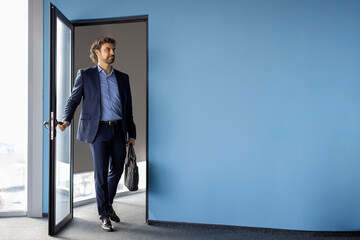 Businessman in business suit successful entrepreneur exits office cabinet mature man opens door end of working day inside company building.