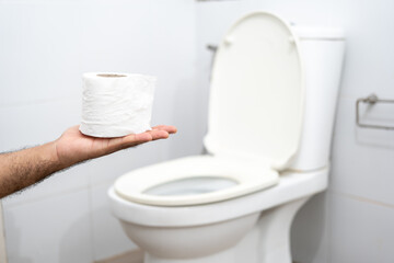 Male suffers from diarrhea holds toilet paper roll in front toilet bowl. Man squeezing tissue with...
