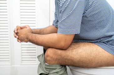 Man suffers from diarrhea having a stiff fist sitting on toilet bowl. Hand holding stomach with...