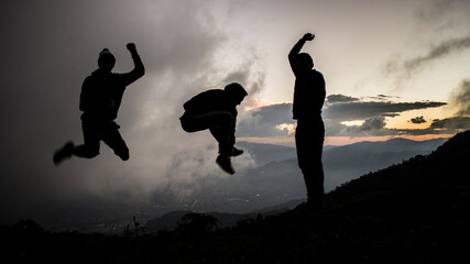 Three friends jumping over a mountains landscape on a cloudy afternoon at the sunset