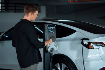 Young man travel with EV electric car to shopping center parking lot charging in downtown city...