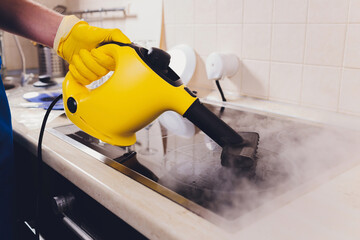 Cleaning kitchen hob with a steam cleaner.