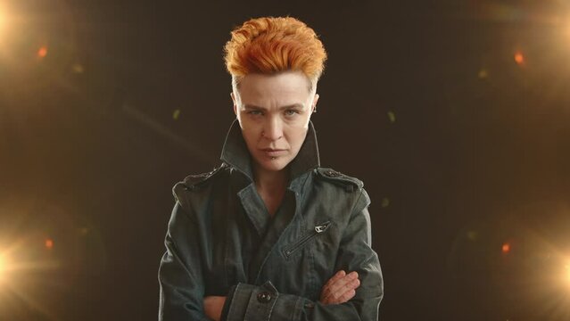A stylish lesbian rocker with distinctive orange hair and facial piercings gives a serious, intense look to the camera, illuminated by bright lights on a dark background. Camera 8K RAW. 