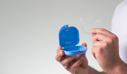 close-up of a young man hands holding transparent dental retainer and a case for their storage and protection. Male hands holding dental teeth aligner, copy space, isolated on light grey color