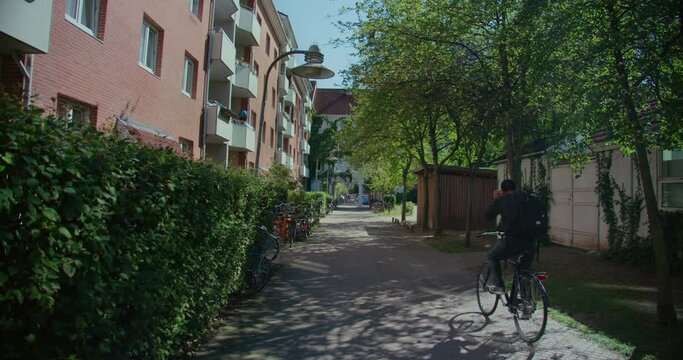 Commuter cyclist pass on a bike on small pedestrian street in Copenhagen residential neighbourhood. Calm and peaceful european lifestyle. Carfree and cycling friendly city 