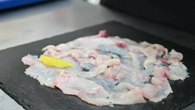 carpaccio di pesce crudo condito da un chef nella cucina di un ristorante di mare