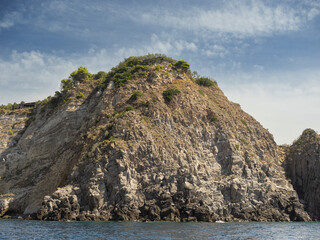 Naklejka premium Weathered seaside rock face texture with parts of green and blue water. Aged volcanic stone wall surface background pattern with cracks and scratches. Banner. Ischia Island, Italy.