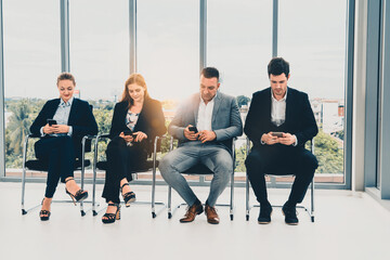 Businesswomen and businessmen using mobile phone while waiting on chairs in office for job...