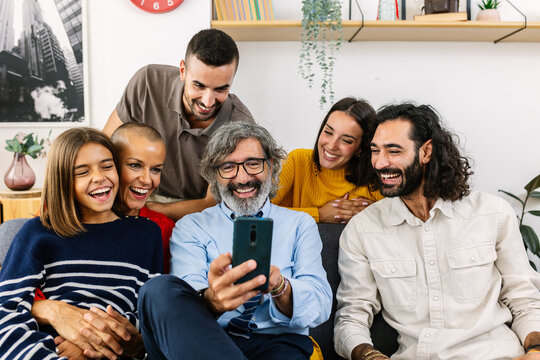 Multi-generational family using mobile phone sitting together on sofa at home. Technology and domestic lifestyle concept.