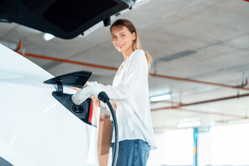 Young woman travel with EV electric car to shopping center parking lot charging in downtown city...