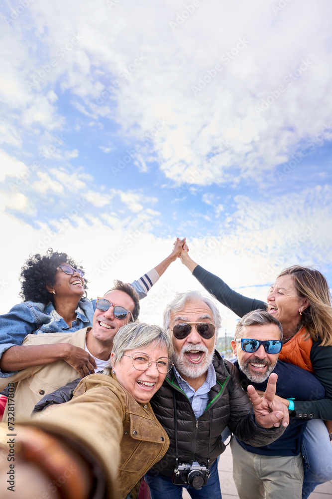 Wall mural vertical group diverse funny mature tourist friends posing piggyback with hands joined in air taking