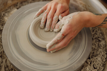 Female potter in apron making shape of clay vase on spinning pottery tool in ceramic workshop