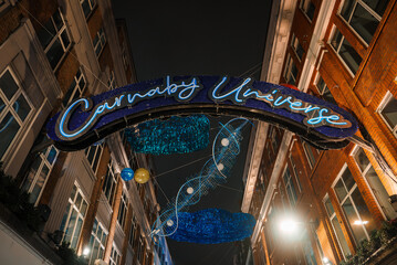 Illuminated Carnaby Universe archway with blue swirling lights captures the festive spirit of Christmas in London, UK, against a backdrop of traditional buildings.