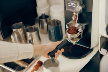 Fototapeta na wymiar Close up of female barista grinding coffee using professional grinder machine in coffee house