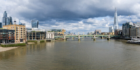 Panorama view east along River Thames in London under moody sky with Southwark Bridge