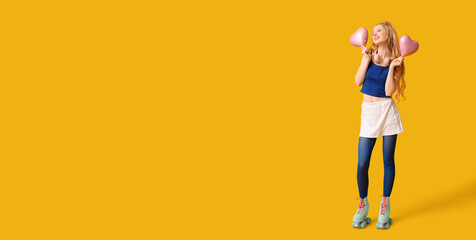 Happy young woman in vintage roller skates and with heart-shaped balloons on yellow background with space for text