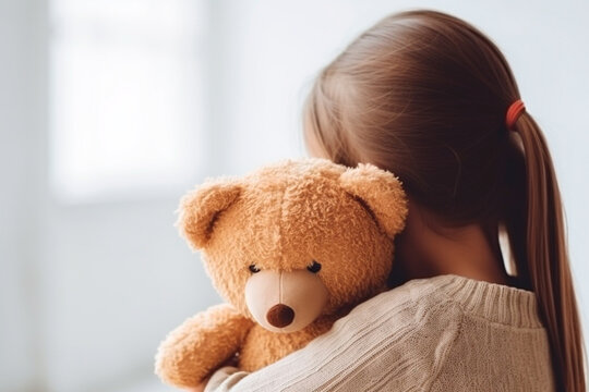 An enchanting image of a shy girl hiding while embracing her teddy bear.
