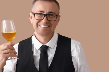 Mature sommelier with glass of wine on beige background, closeup
