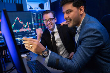 Two stock exchange traders discussing on dynamic successful investment graph, pointing trending of high profit in currency stock in financial data on monitor in neon light at workplace. Sellable.