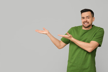 Handsome worried young man pointing at something on grey background