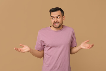 Handsome ashamed young man shrugging on brown background