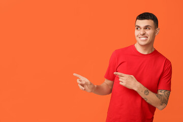Handsome ashamed young man pointing at something on orange background