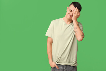 Handsome ashamed young man covering face with hand on green background