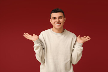 Handsome ashamed young man shrugging on red background