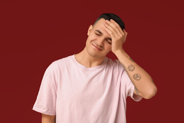 Handsome ashamed young man covering face with hand on red background