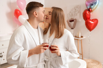 Beautiful young couple in bathrobes with glasses of wine celebrating Valentine's Day at home