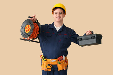 Male electrician with extension cord reel and bag of tools on beige background
