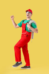 Happy electrician with extension cord on yellow background