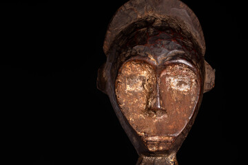Fototapeta na wymiar An African male figure portrait carved in wood isolated on black. Traditional African art with balanced shapes and volumes and beautiful black patina and kaolin pigments.