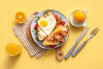Composition with tasty fried egg, cut croissant, bacon, tomatoes and glass of juice on yellow background