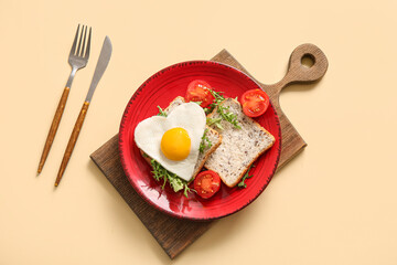 Plate with tasty fried egg, toasts, tomatoes, arugula and cutlery on beige background