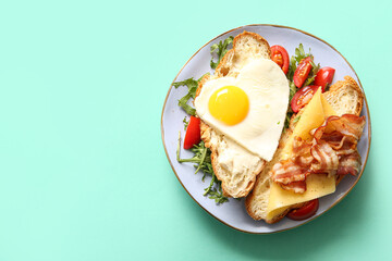 Plate with tasty fried egg, cut croissant, tomatoes and arugula on turquoise background