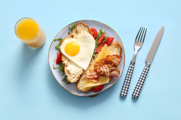 Plate with tasty fried egg, cut croissant, tomatoes and glass of juice on blue background