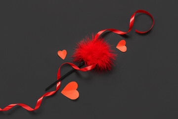Composition with feather stick from sex toys, paper hearts and red ribbon on dark background....