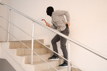 Male thief with crowbar and gun in stairway