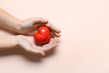 Female hands holding red heart on pink background