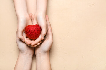 Hands of woman and child with red heart made of string on beige background