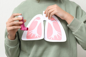 Young woman with paper lungs and asthma inhaler on white background