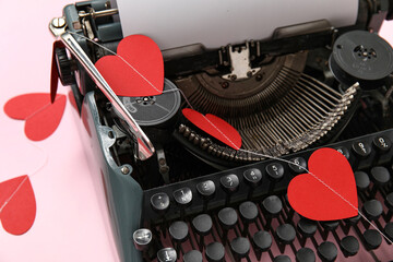 Vintage typewriter and paper hearts for Valentine's day on pink background, closeup