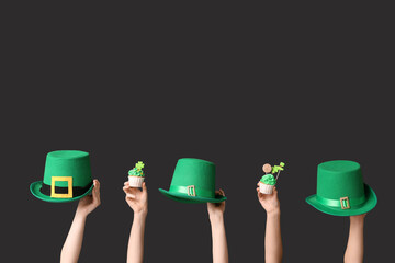 Female hands with tasty cupcakes and leprechaun hats for St. Patrick's Day on black background