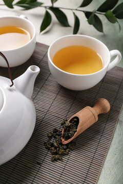 Bamboo mat with teapot, cups of tea and dry leaves on green grunge background