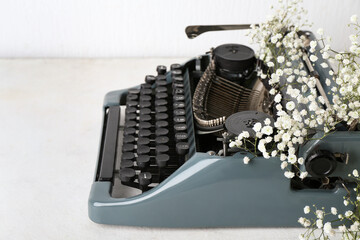 Vintage typewriter and flowers on grunge table near white wall