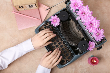 Female hands with vintage typewriter, flowers and calendar on beige grunge background....