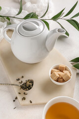 Teapot and spoon with dry tea on light background