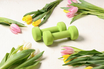 Composition with dumbbells and beautiful tulip flowers on light background